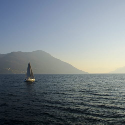 A small sailing boat in the lake with the sunset in the background